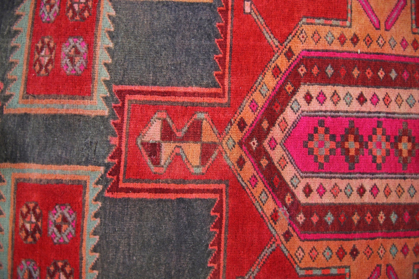A vintage Persian rug featuring geometric patterns in shades of red, pink, and dark grey.