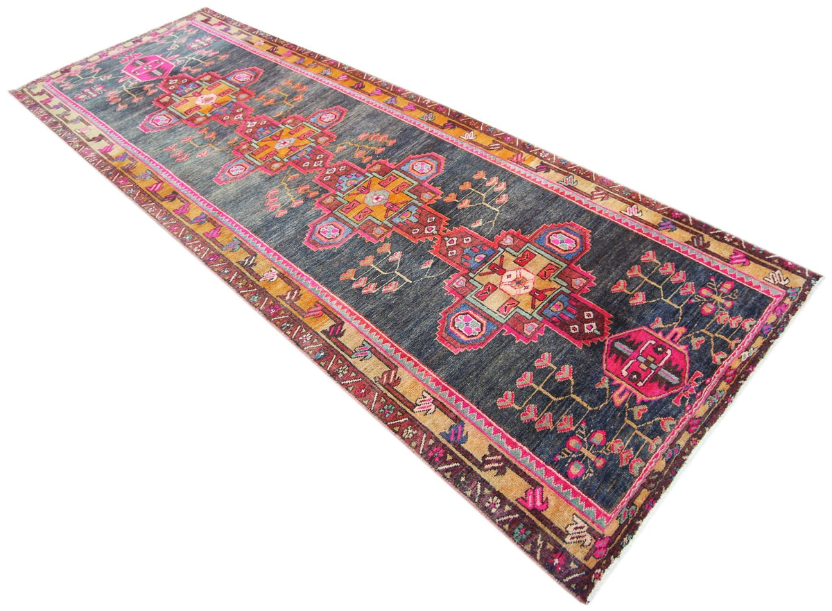 Vintage Persian Lori runner with geometric diamond medallions in pink, orange, and blue on a dark wool field.