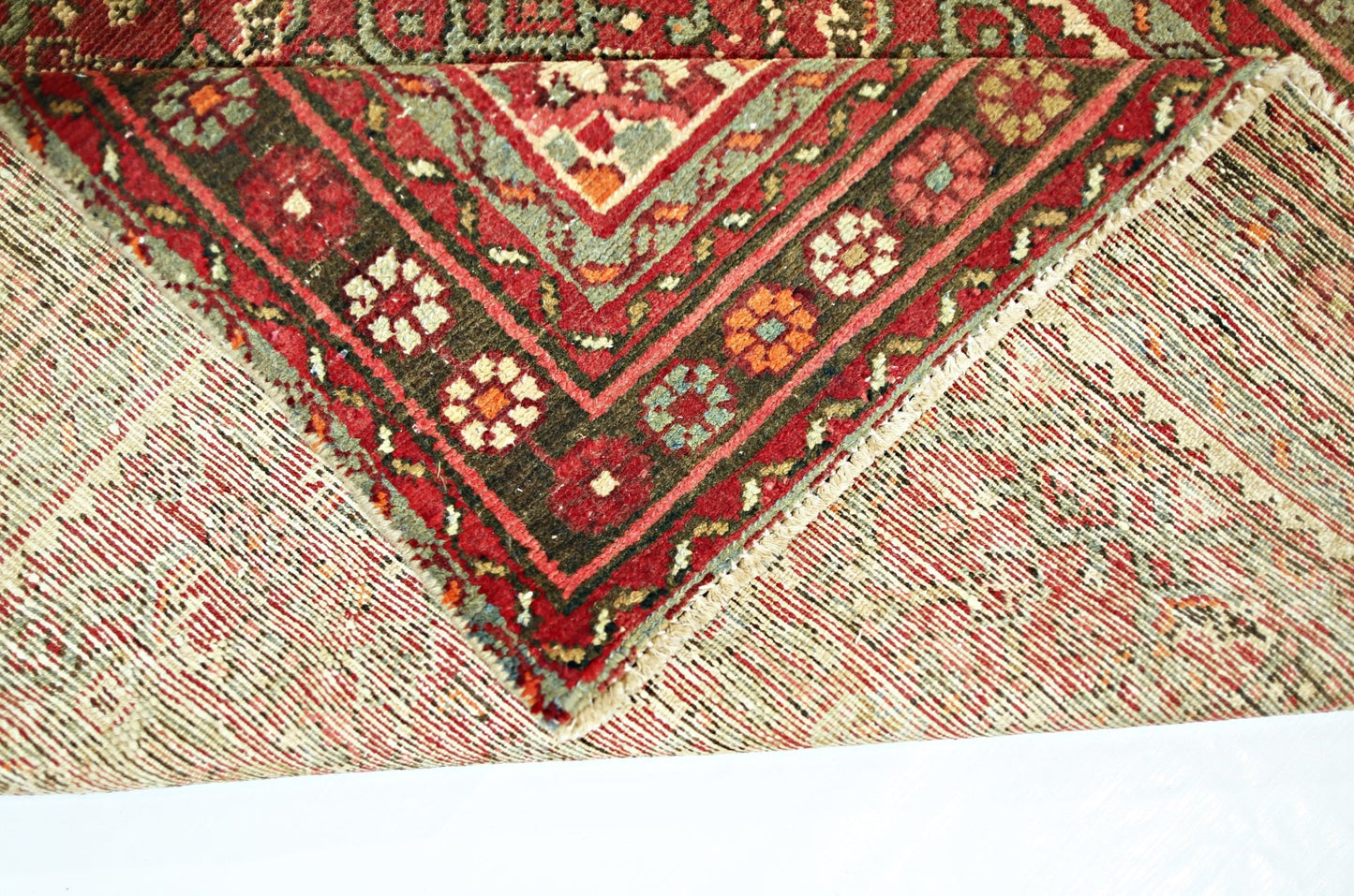 A corner of a vintage Persian Hamadan runner showing its intricate red and green wool pattern.