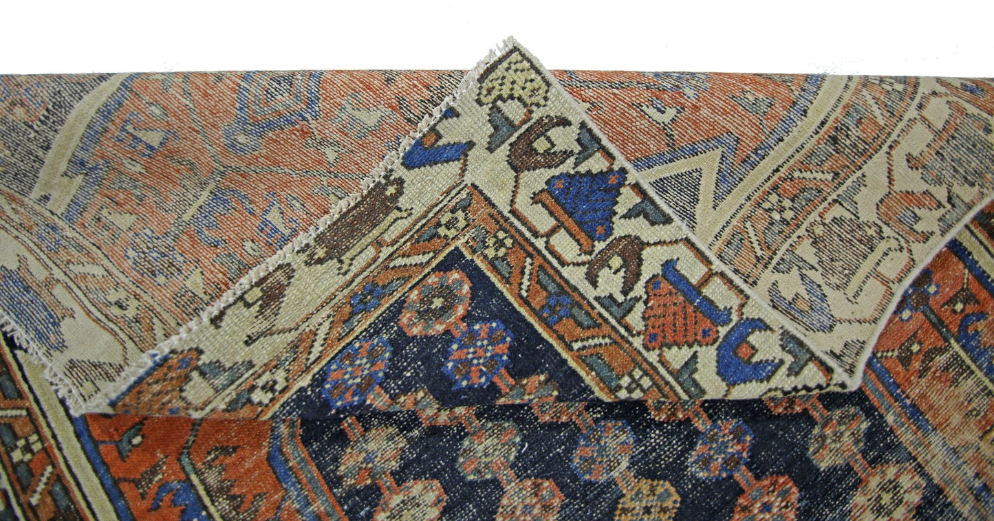A corner of a vintage Persian Mazlaghan rug showing its intricate blue and orange geometric pattern.