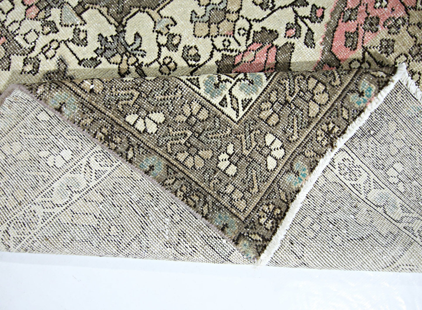 A vintage handmade Persian rug with a floral pattern in muted tones of pink, blue, and brown.