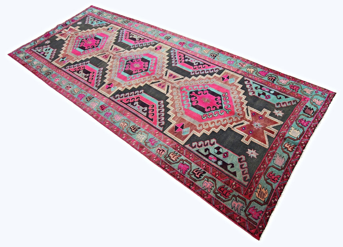 A vintage Persian Ardabil runner featuring geometric patterns in vibrant pink, teal, and charcoal.