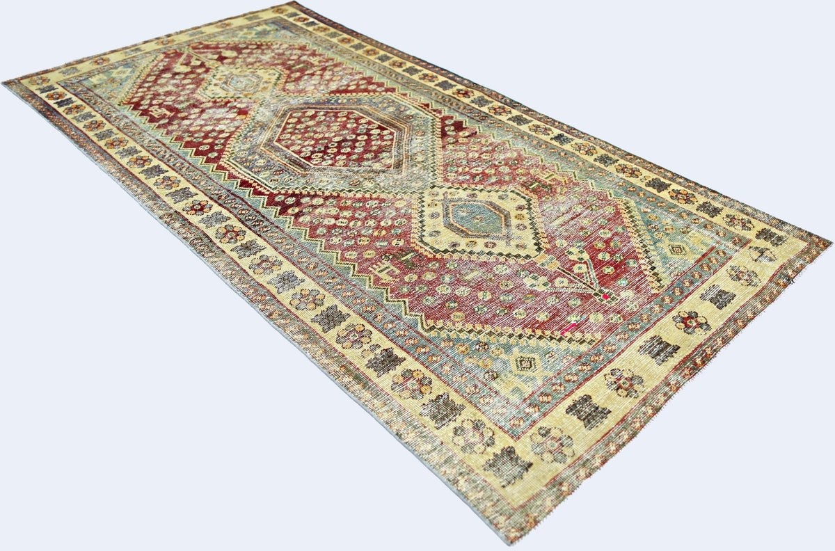 A vintage Persian Qashqai rug featuring a geometric medallion pattern in red, blue, and beige.