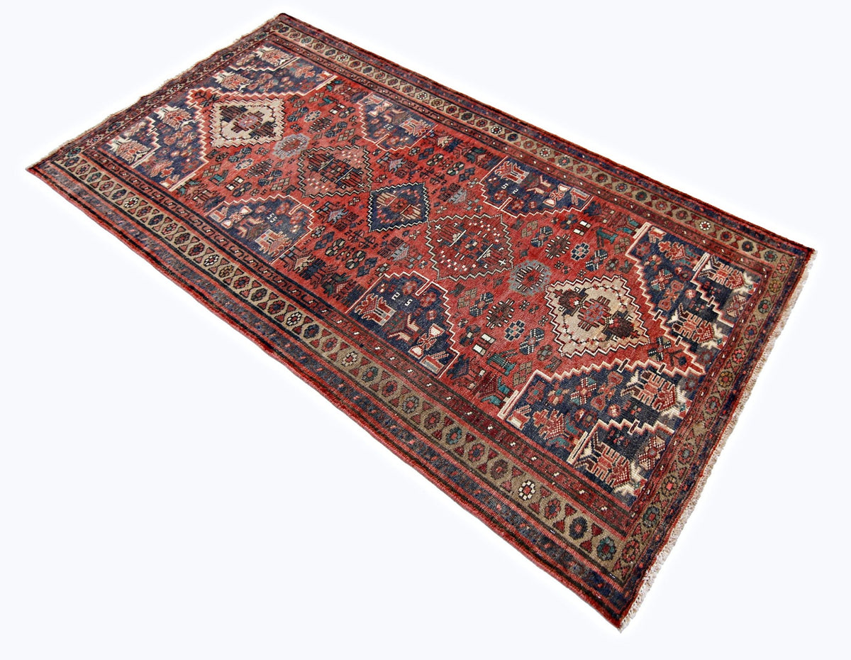 Vintage Persian Qashqai runner with red field, tribal diamond medallions, and intricate geometric motifs on a white background.