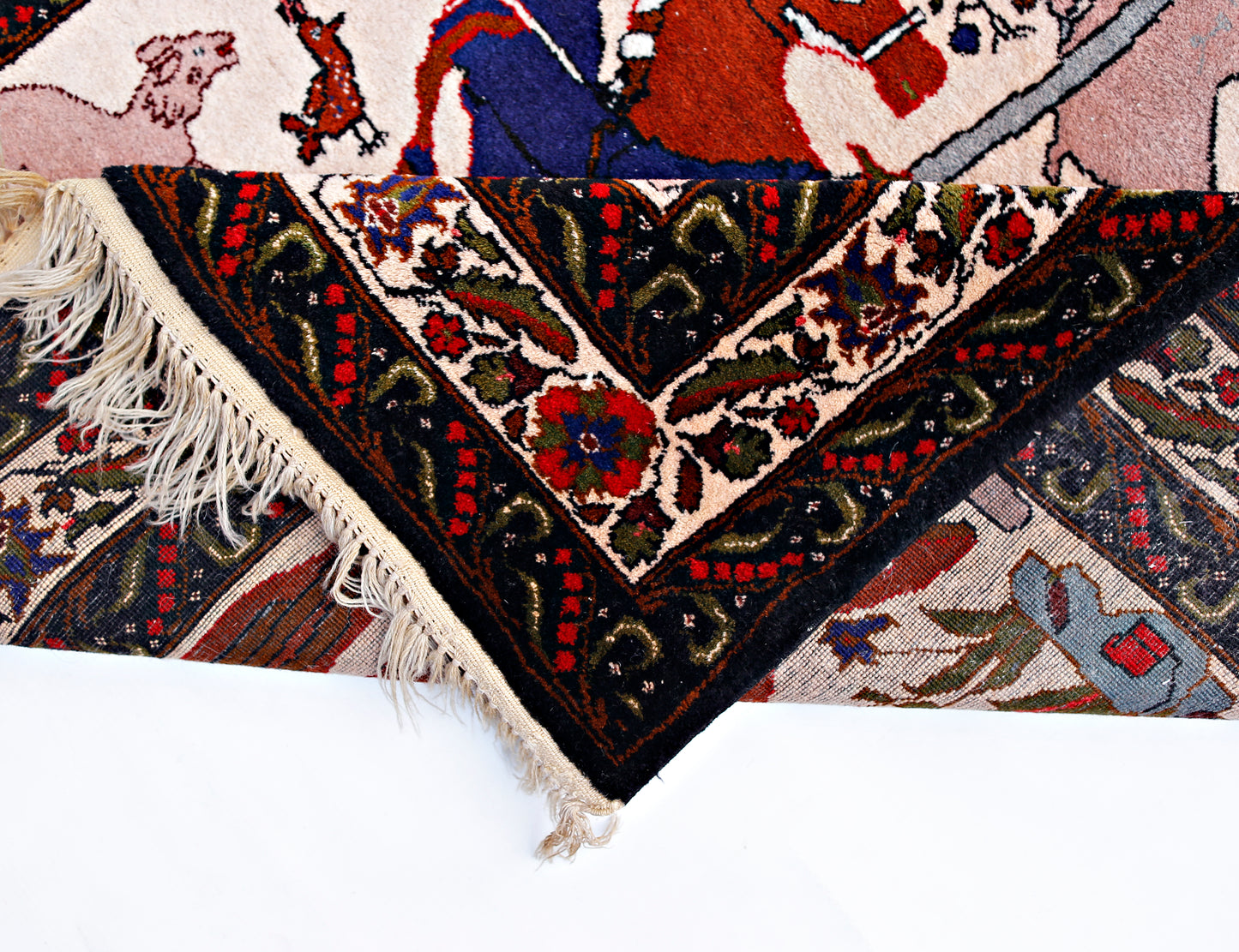 A vintage Persian rug with a hunting scene pattern, featuring a folded corner and fringe.