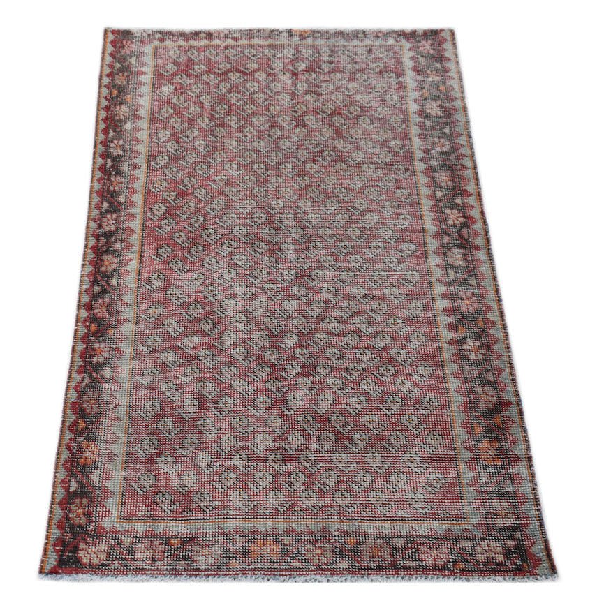 A rectangular vintage Persian rug featuring a red geometric pattern and a decorative border.