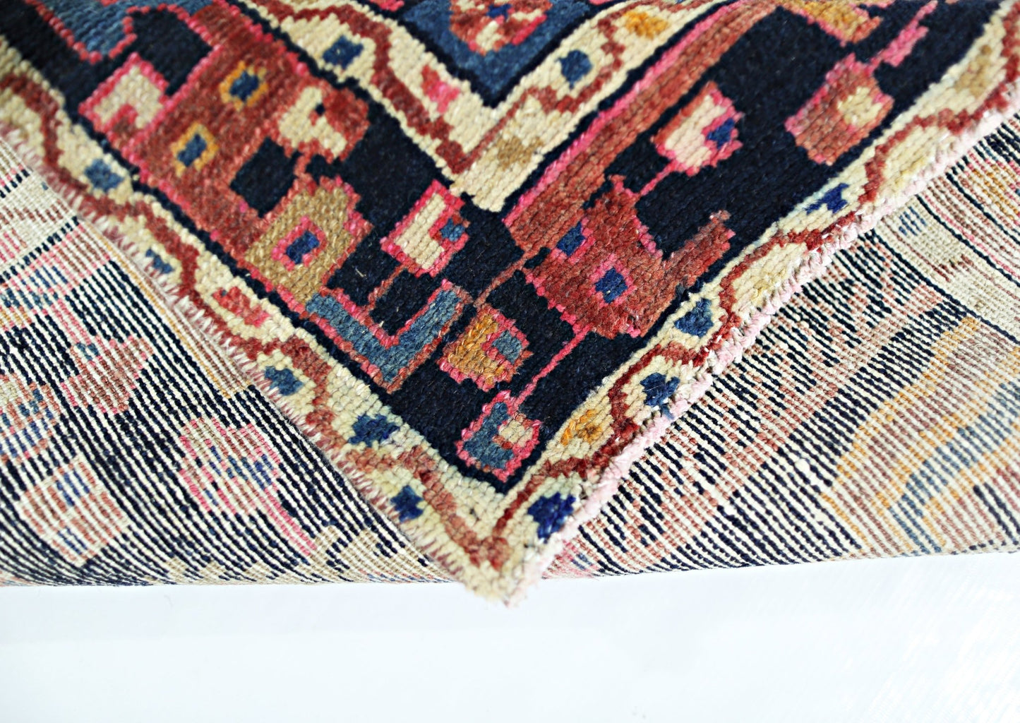 A corner of a vintage handmade Persian wool rug showing its intricate geometric pattern and weave.