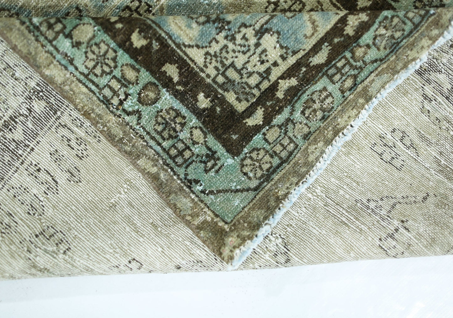 A corner of a vintage Persian wool rug folded over to show its intricate blue and brown pattern.