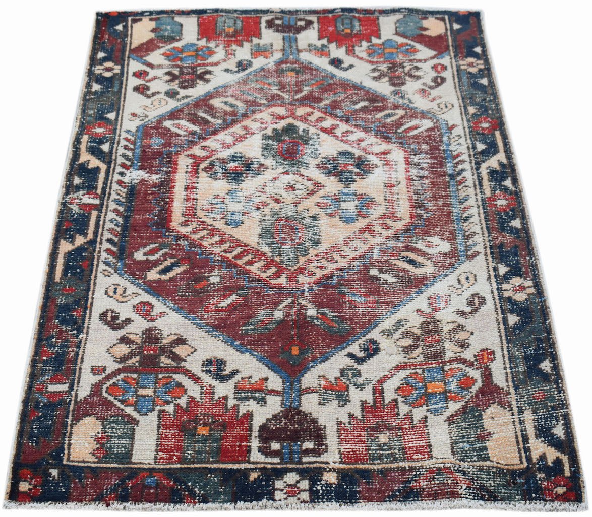 A handwoven vintage Persian rug featuring a central geometric medallion in red, blue, and cream.