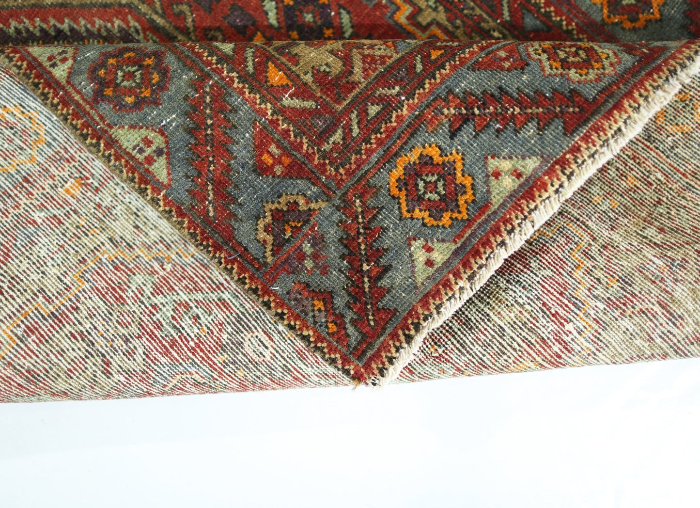 A folded vintage Persian rug featuring intricate geometric patterns in red, blue, and orange.