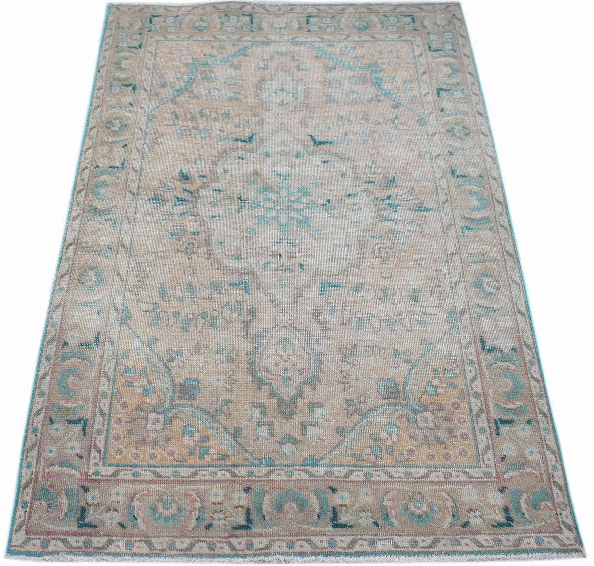 A vintage handwoven Persian rug featuring a faded floral medallion pattern in beige and teal.