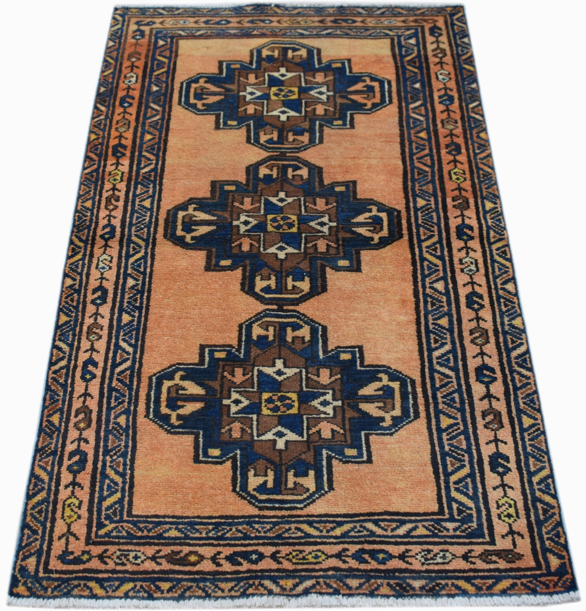 A handwoven vintage Persian rug featuring three blue and brown geometric medallions on an orange field.