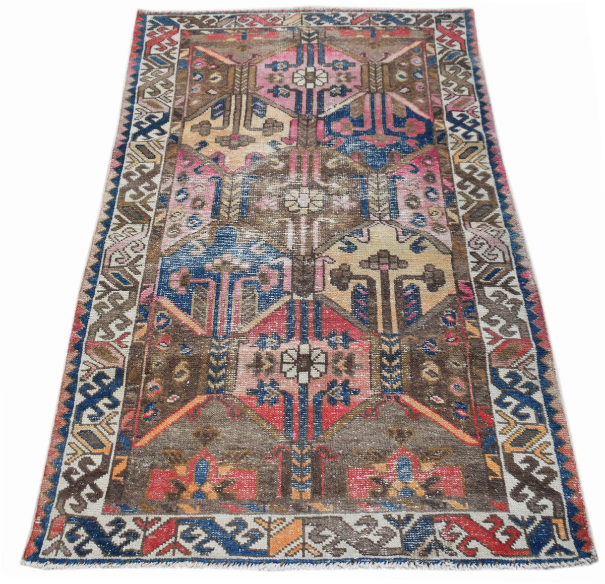 A vintage handwoven Persian rug featuring a geometric pattern in shades of blue, pink, and brown.