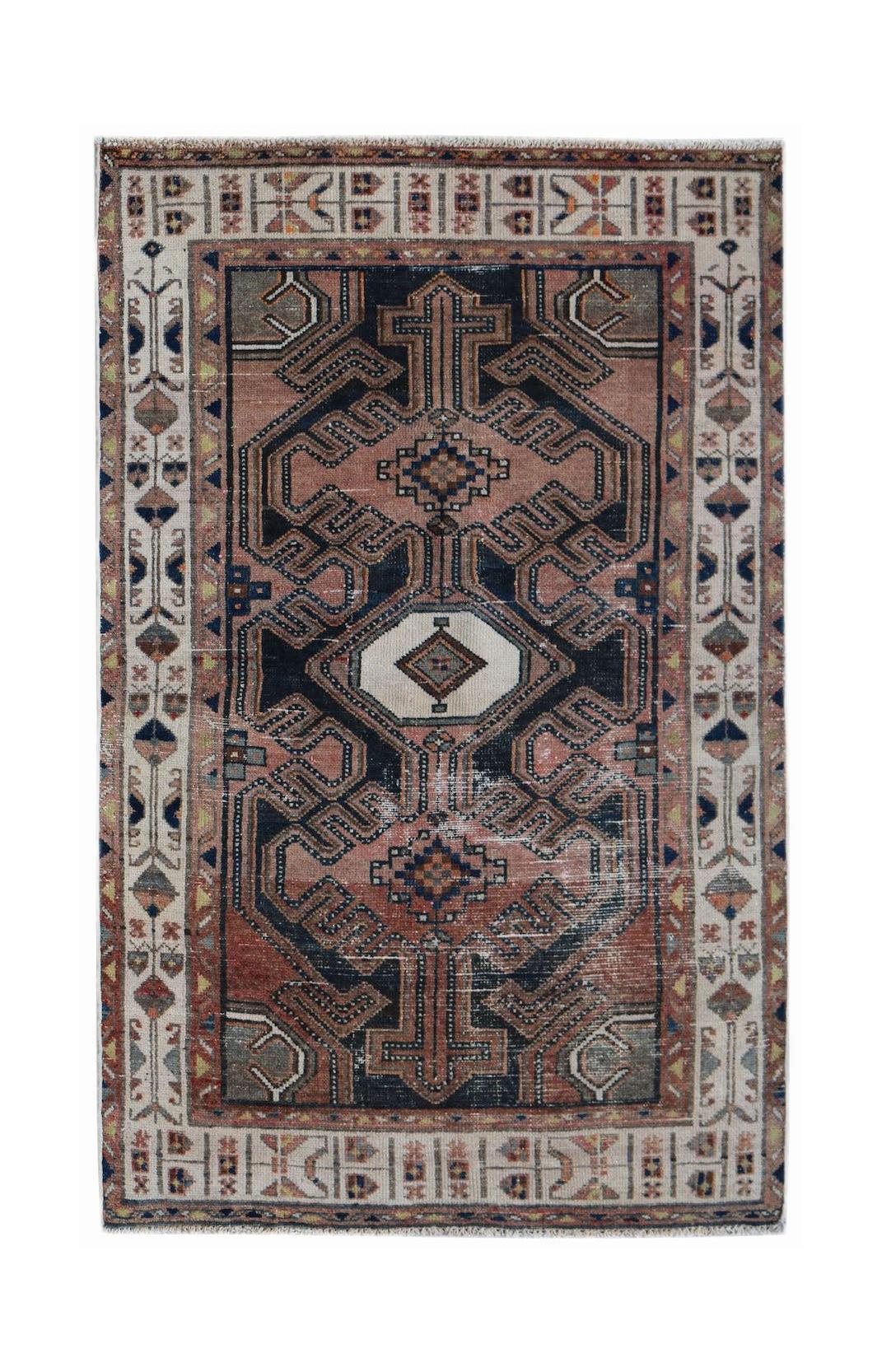 A vintage handwoven Persian rug featuring a geometric medallion pattern in muted red and navy tones.