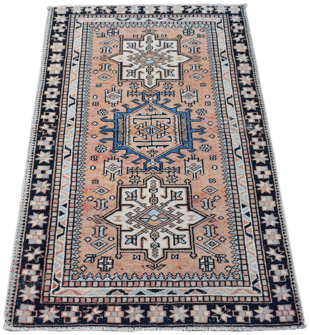 A handwoven vintage Persian rug featuring a geometric pattern in peach, blue, and cream tones.