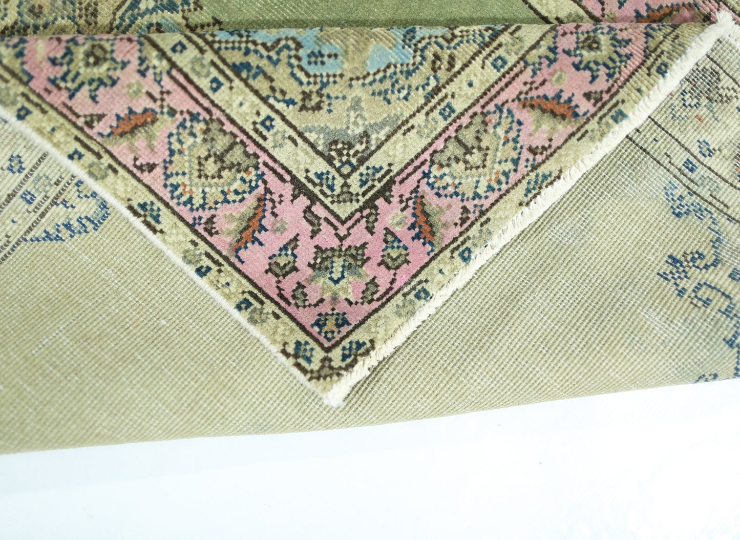 A corner of a vintage handmade Persian rug with a pink floral border and green wool pile.