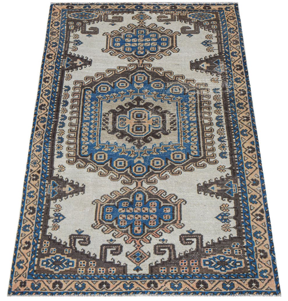 Vintage Persian rug with a light background and intricate blue, brown, and tan geometric patterns.