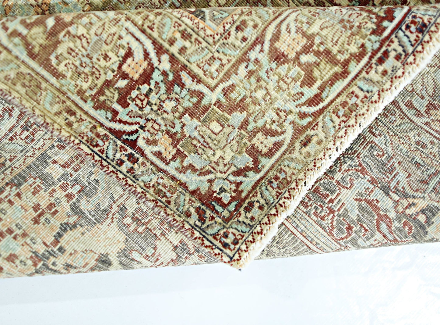 A folded vintage Persian rug featuring intricate patterns in shades of red, blue, and beige.