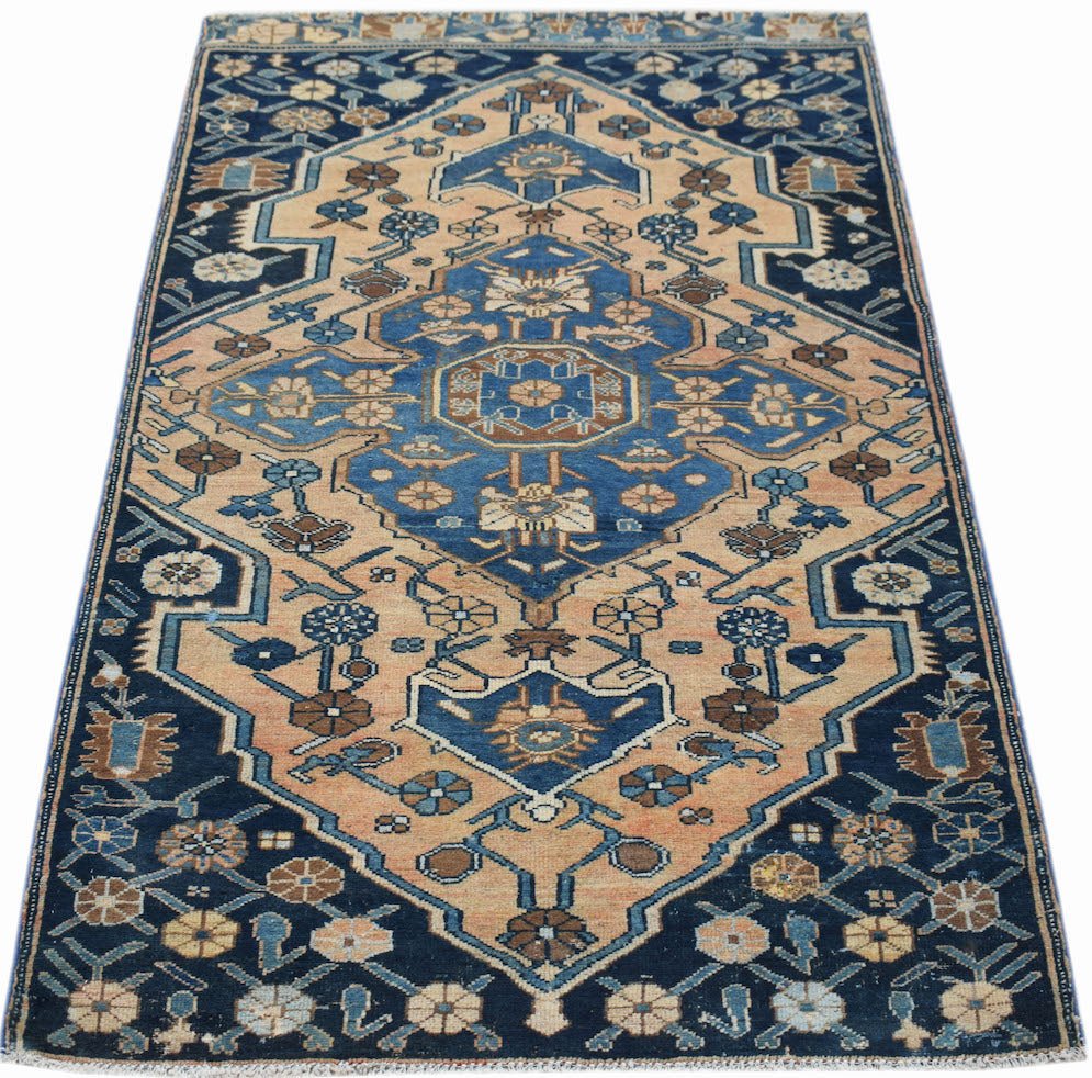 A handwoven vintage Persian rug featuring a geometric floral pattern in blue and tan tones.