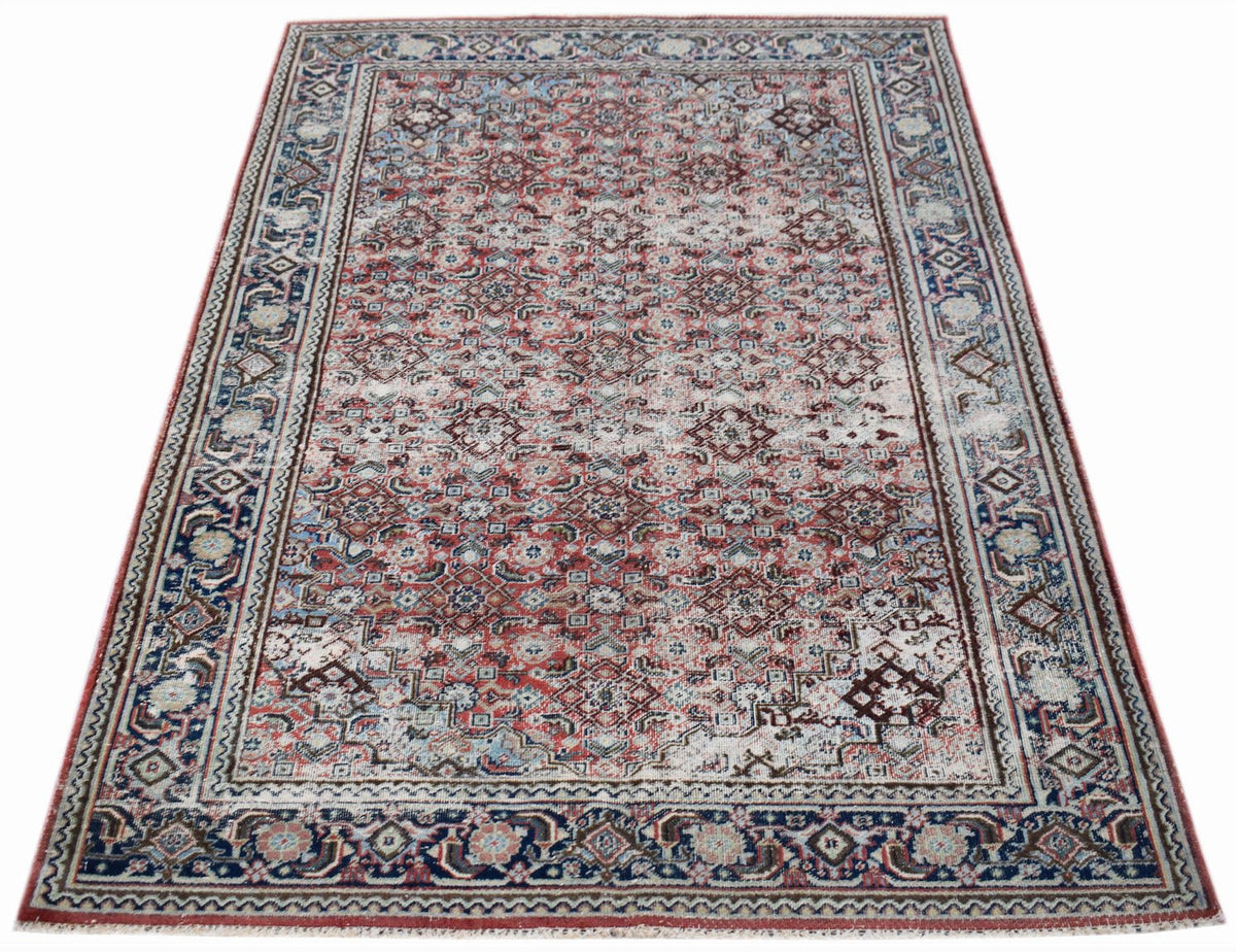 A vintage handwoven Persian rug featuring a faded red and blue geometric pattern.