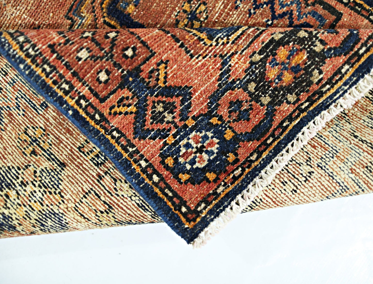 A folded vintage Persian rug featuring intricate geometric patterns in red, blue, and cream.