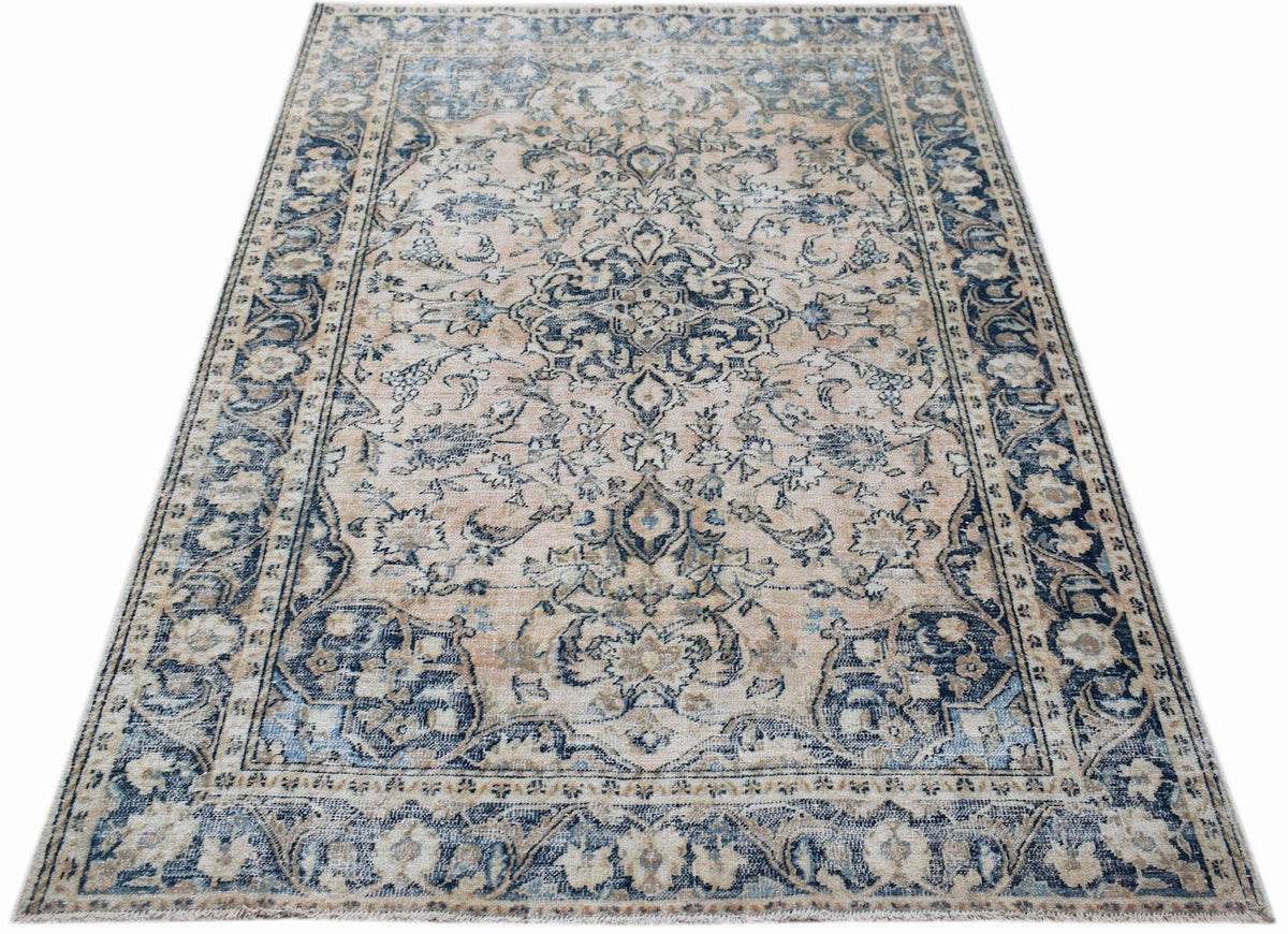 A vintage handwoven Persian rug featuring a faded floral pattern in shades of blue and beige.