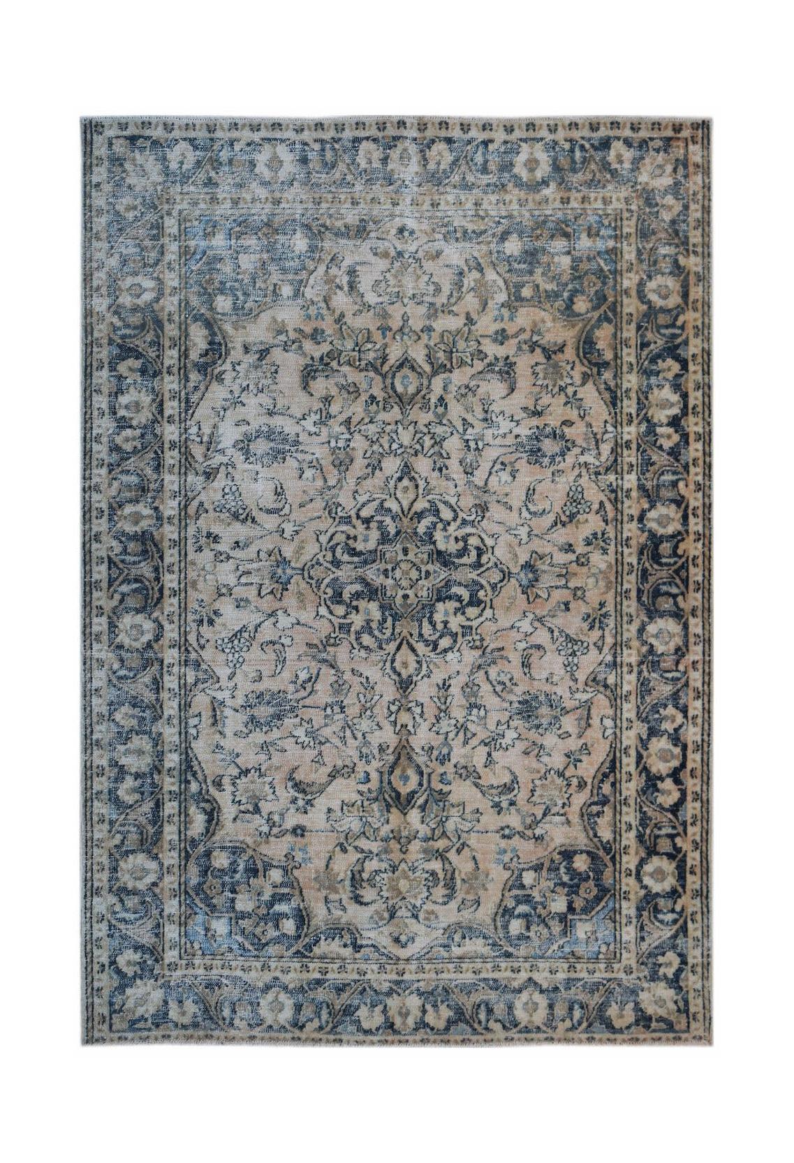 A vintage handwoven Persian rug featuring a faded floral medallion pattern in blue and beige.