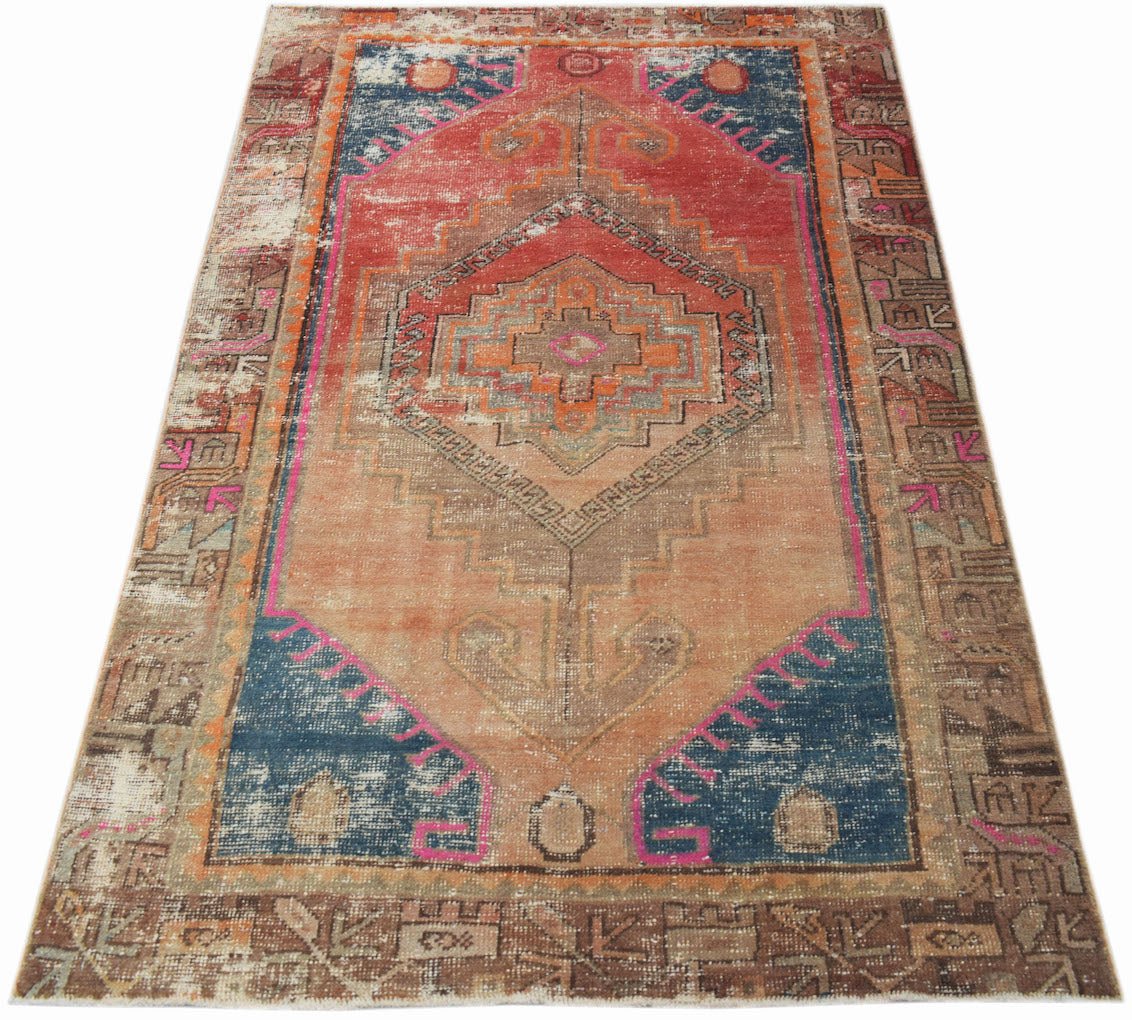 A vintage handwoven Persian rug featuring a geometric medallion pattern in orange, blue, and pink.