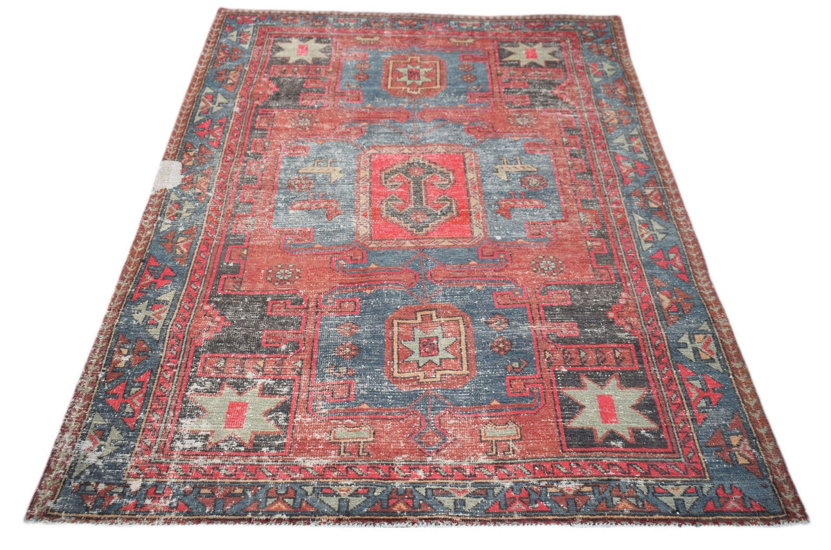 A vintage handwoven Persian rug featuring a distressed red and blue geometric pattern.