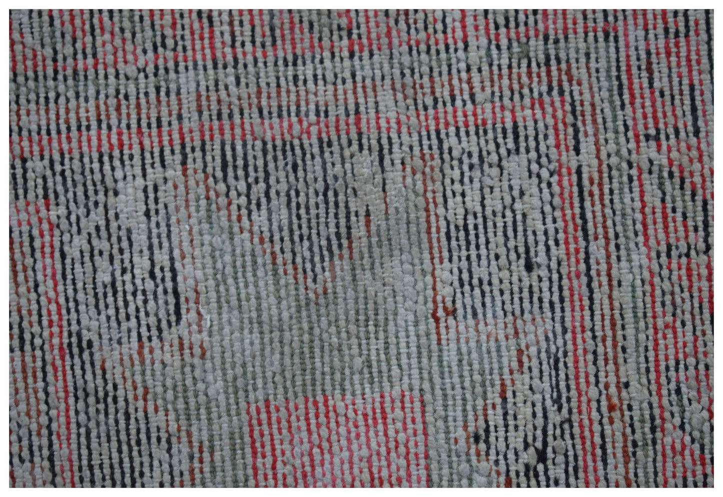 A close-up of a handwoven vintage Persian rug featuring a faded geometric pattern in red and grey.