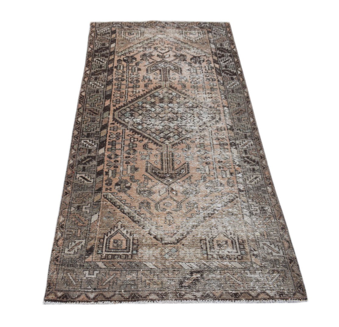 A handwoven vintage Persian rug featuring a faded geometric diamond pattern in muted earth tones.