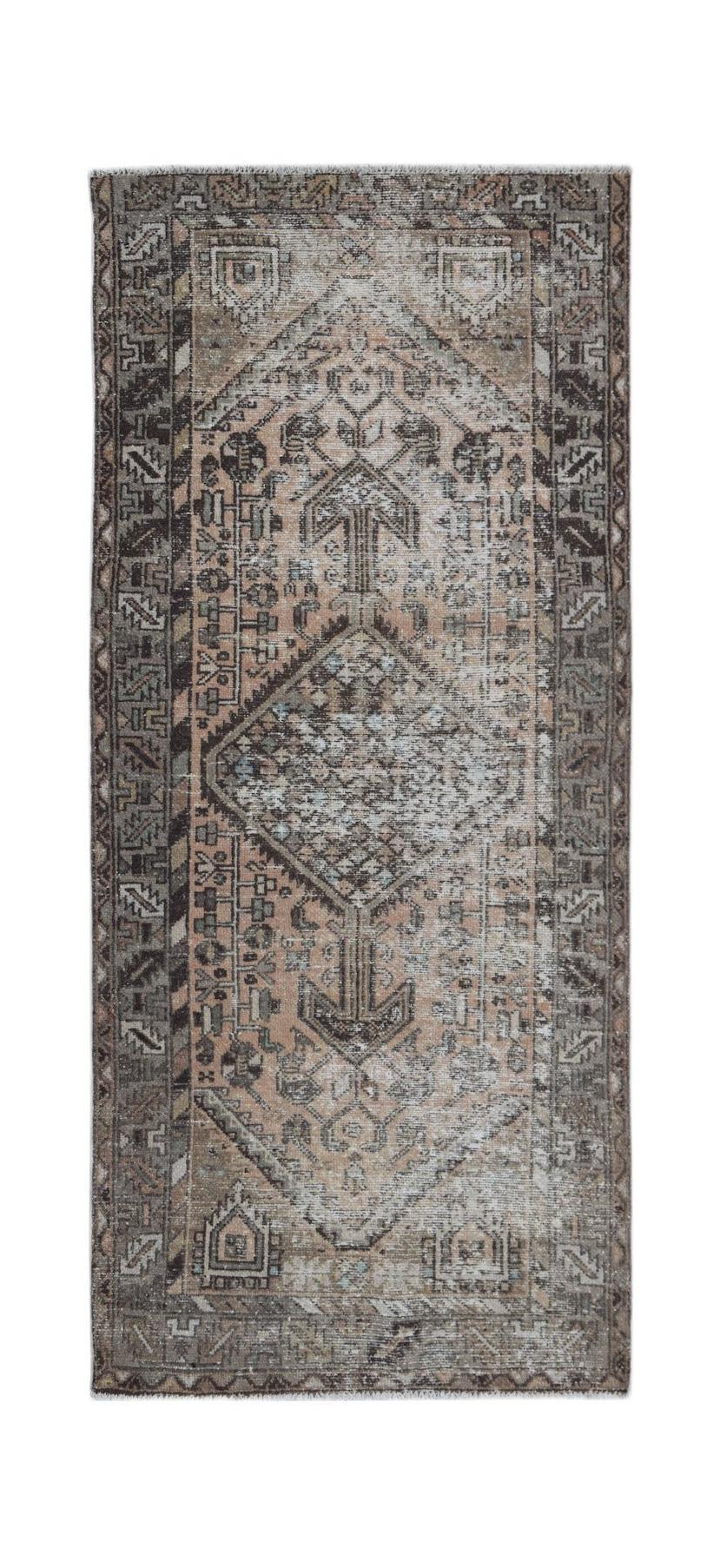 A handwoven vintage Persian rug featuring a faded geometric diamond pattern in muted earth tones.