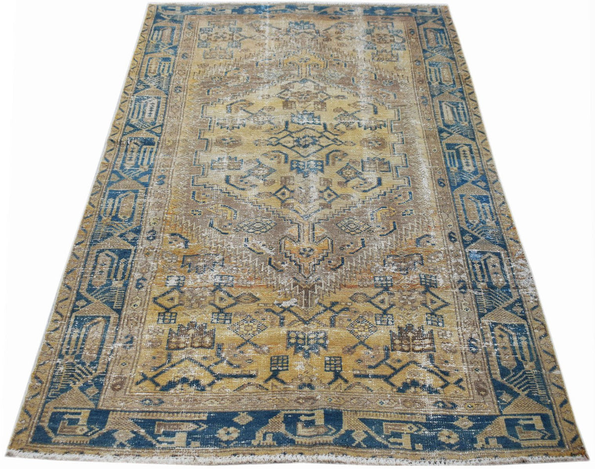 A rectangular vintage Persian rug featuring a distressed geometric pattern in blue and gold tones.