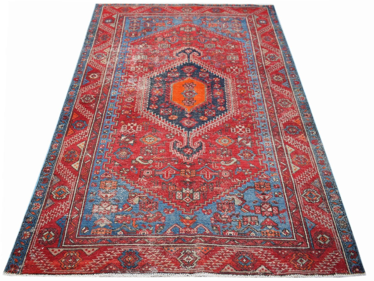 A handwoven vintage Persian rug featuring a central orange medallion on a red and blue field.