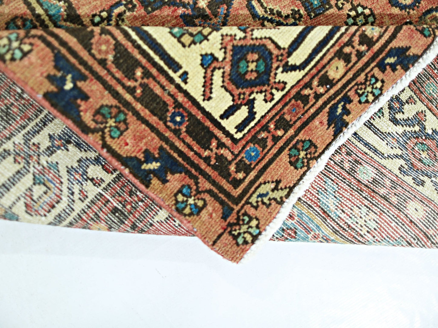 A folded vintage Persian rug featuring intricate geometric patterns in red, blue, and cream tones.