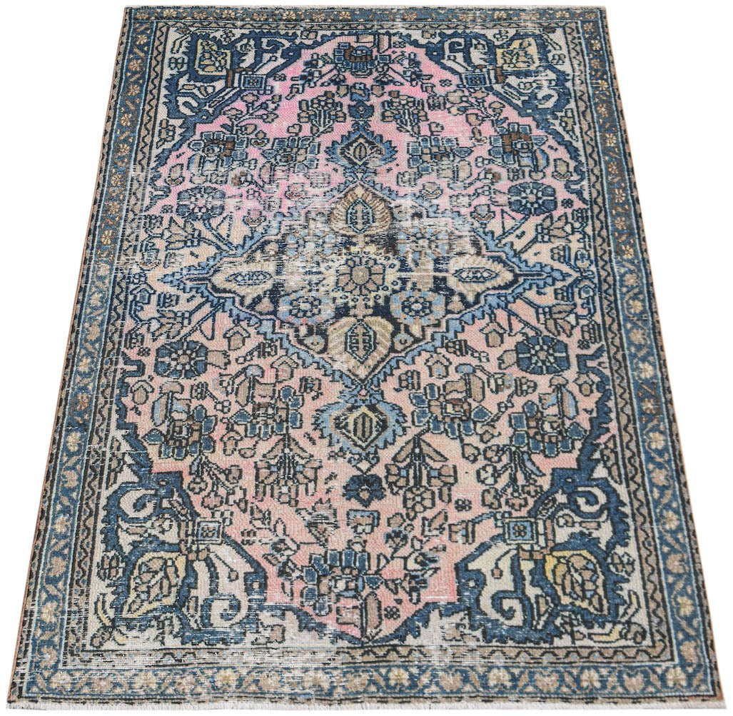 A vintage handwoven Persian rug featuring a central medallion pattern in shades of pink and blue.