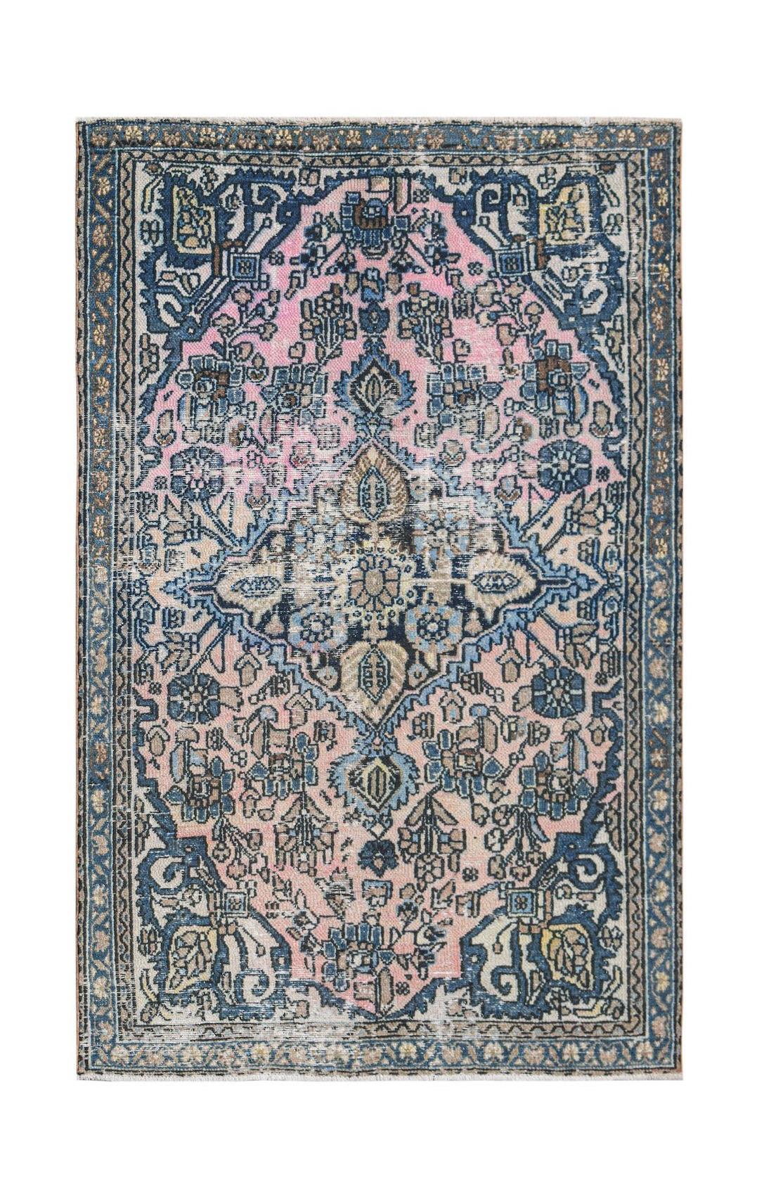 A vintage handwoven Persian rug featuring a floral medallion pattern in pink, blue, and cream.