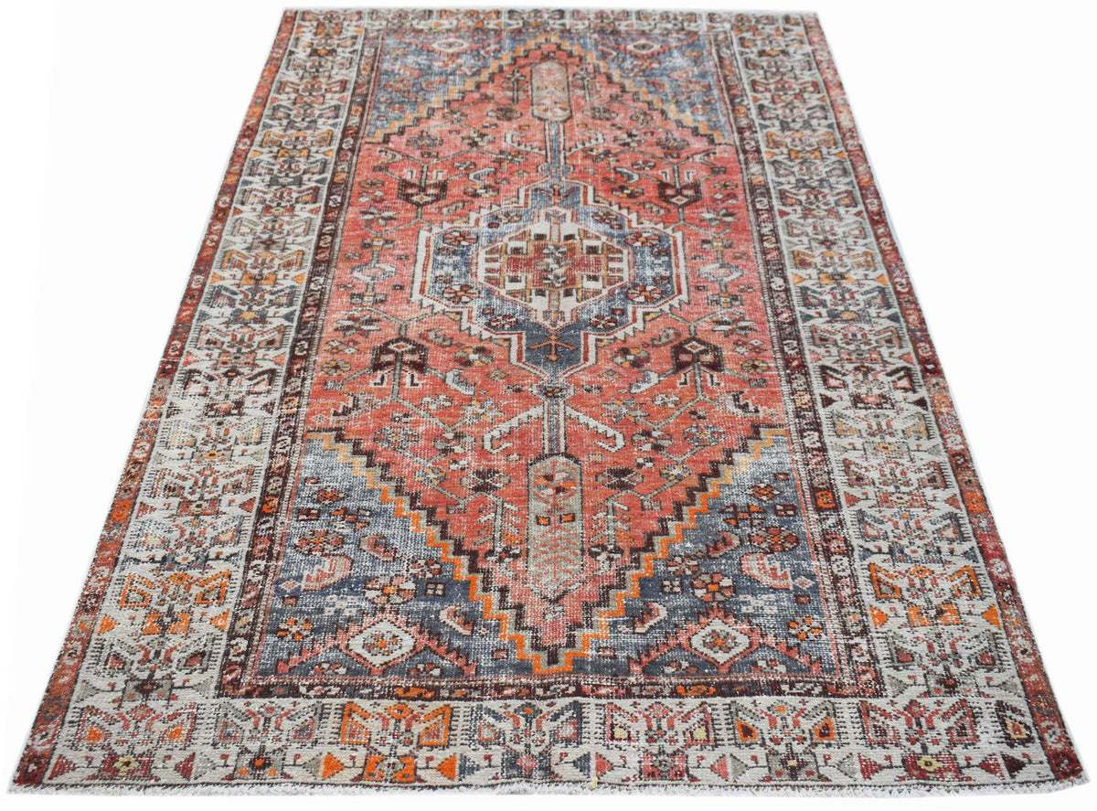 A vintage handwoven Persian rug featuring a geometric medallion pattern in red, blue, and cream.