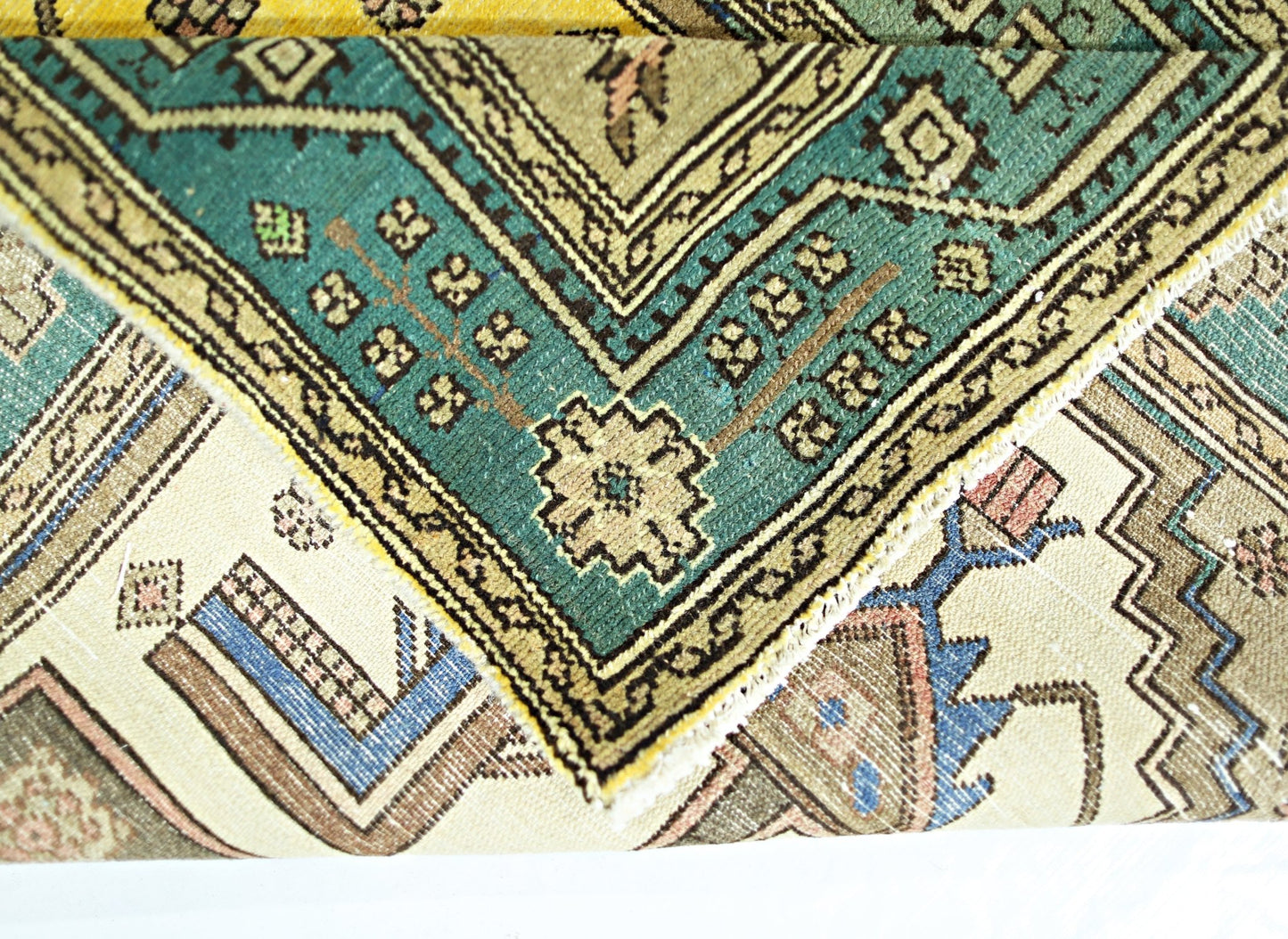 A folded vintage Persian rug featuring intricate geometric patterns in teal, beige, and blue.
