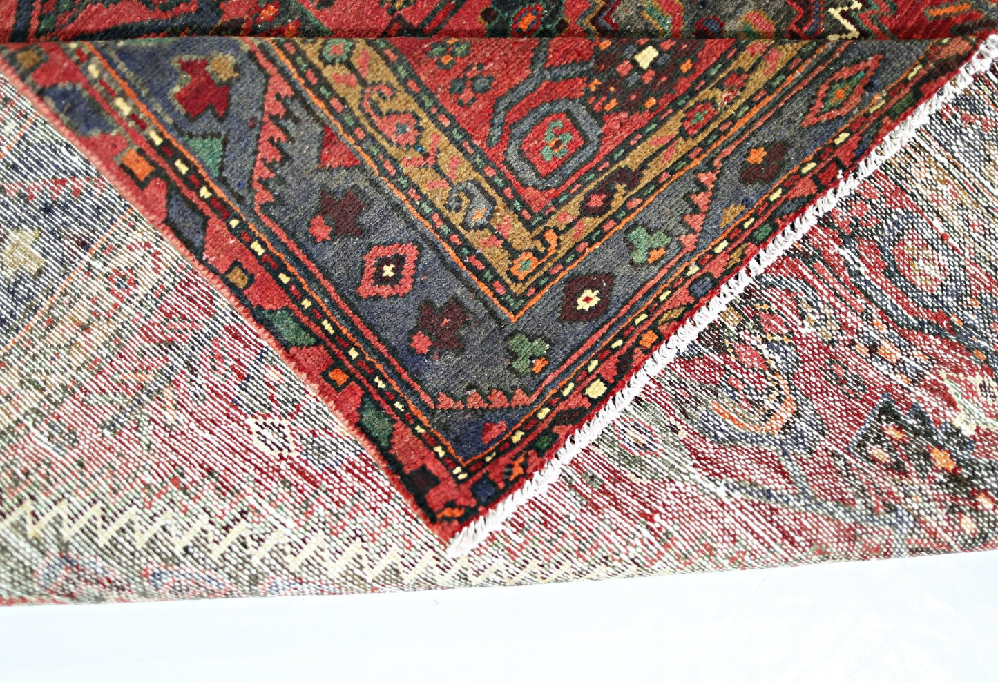 A corner of a vintage Persian rug folded over to show its intricate red and blue wool pattern.