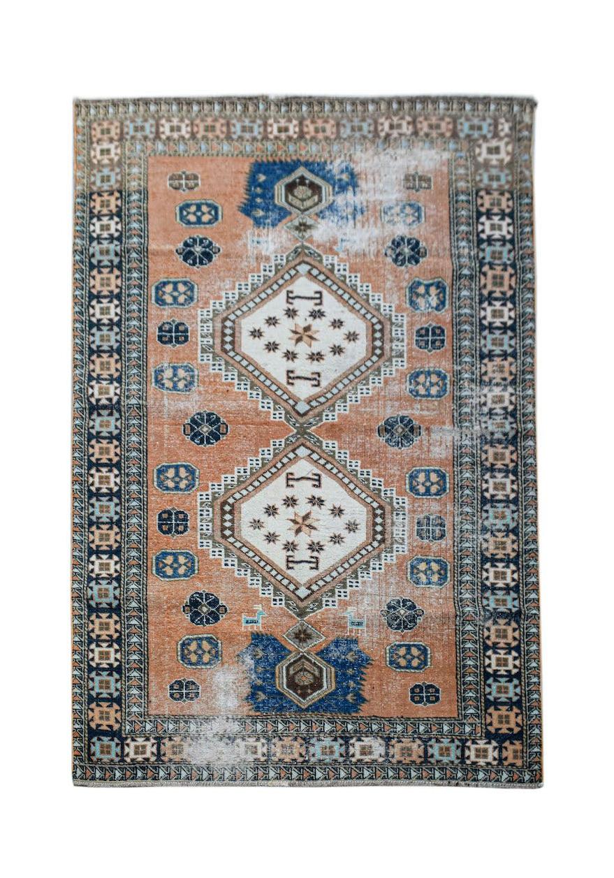A vintage handwoven Persian rug featuring a geometric pattern in orange and blue tones.