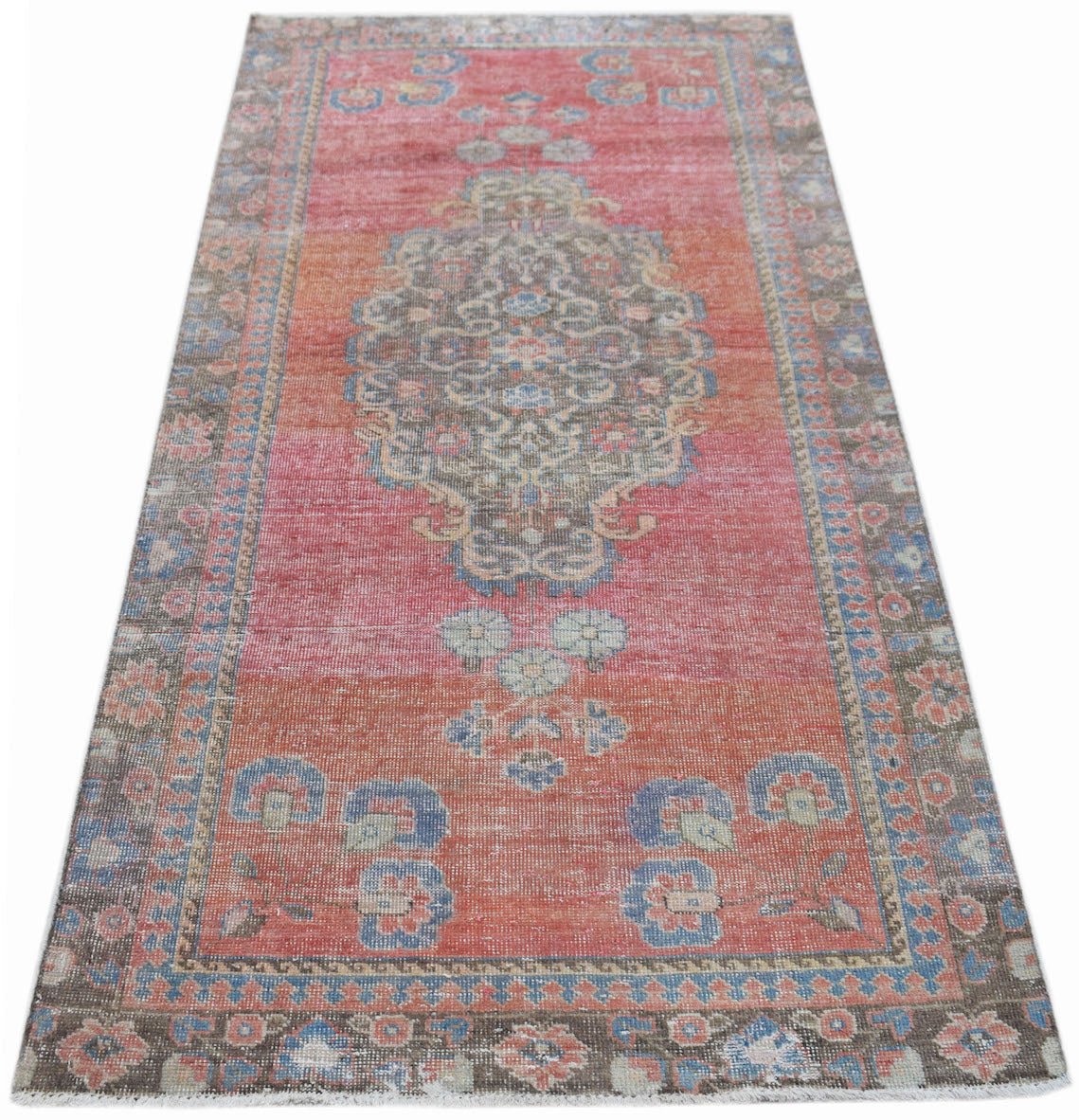 A vintage handwoven Persian rug featuring a faded red and orange floral medallion pattern.