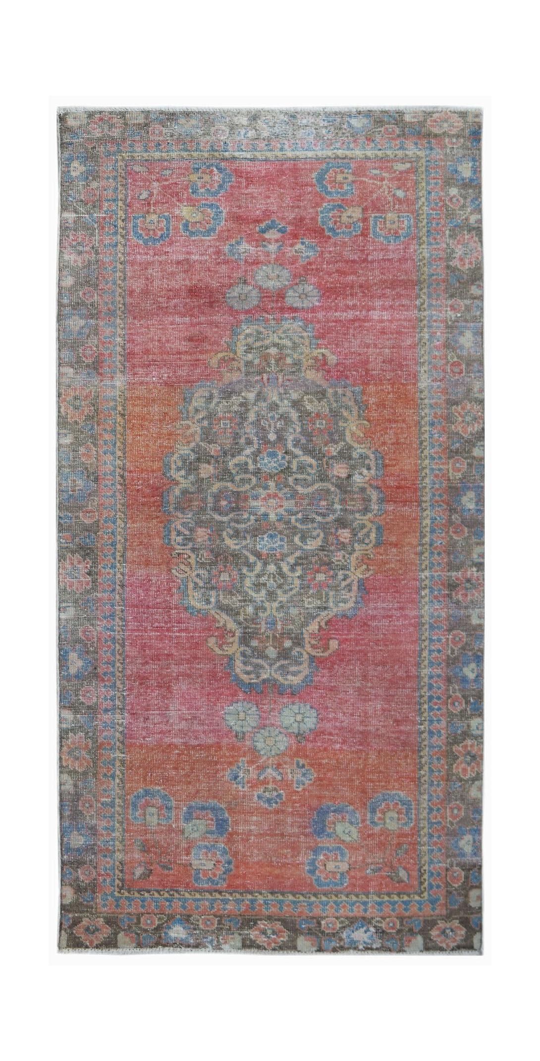 A vintage handwoven Persian rug featuring a central medallion on a faded red and orange field.