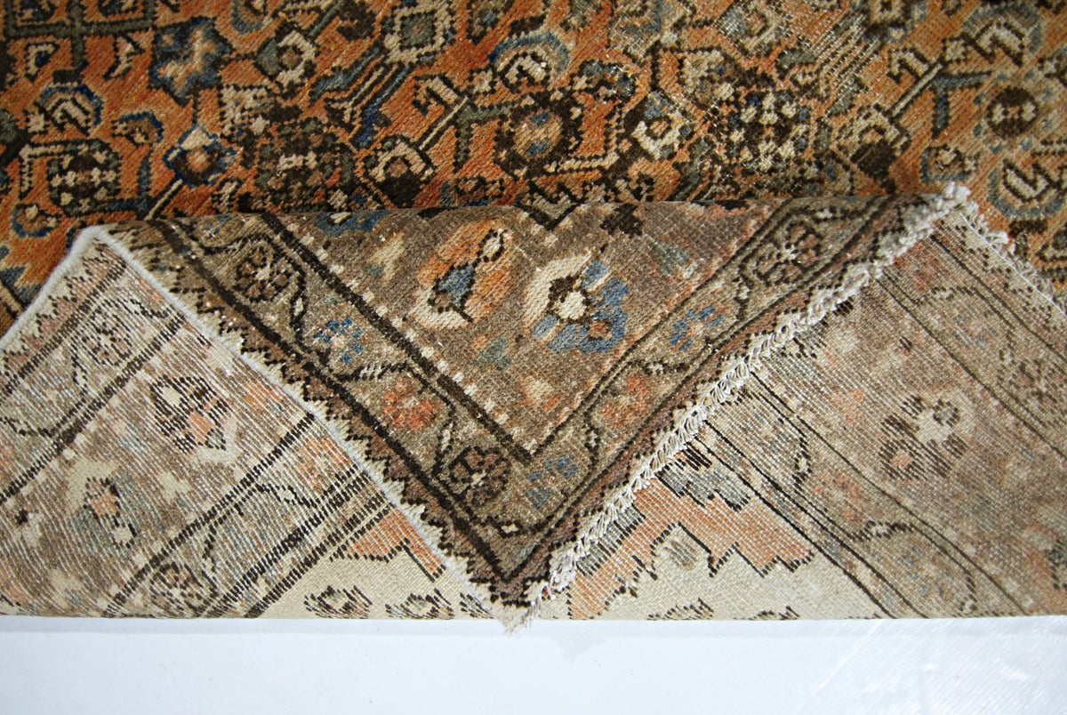 A vintage Persian rug with a folded corner revealing its intricate floral pattern and wool texture.