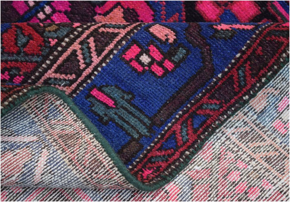 A corner of a handmade vintage Persian wool rug showing its vibrant blue, pink, and red pattern.