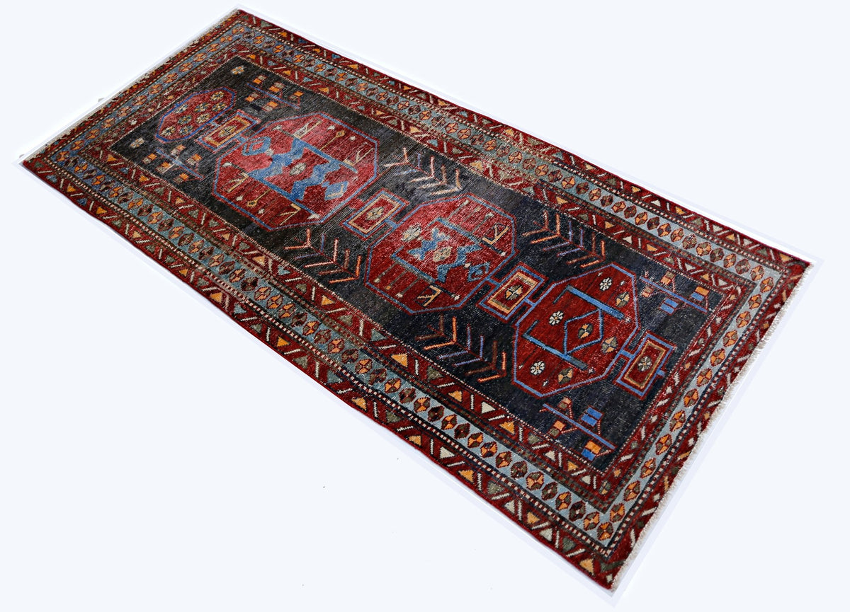 A rectangular vintage Persian rug featuring geometric red medallions on a dark charcoal field.