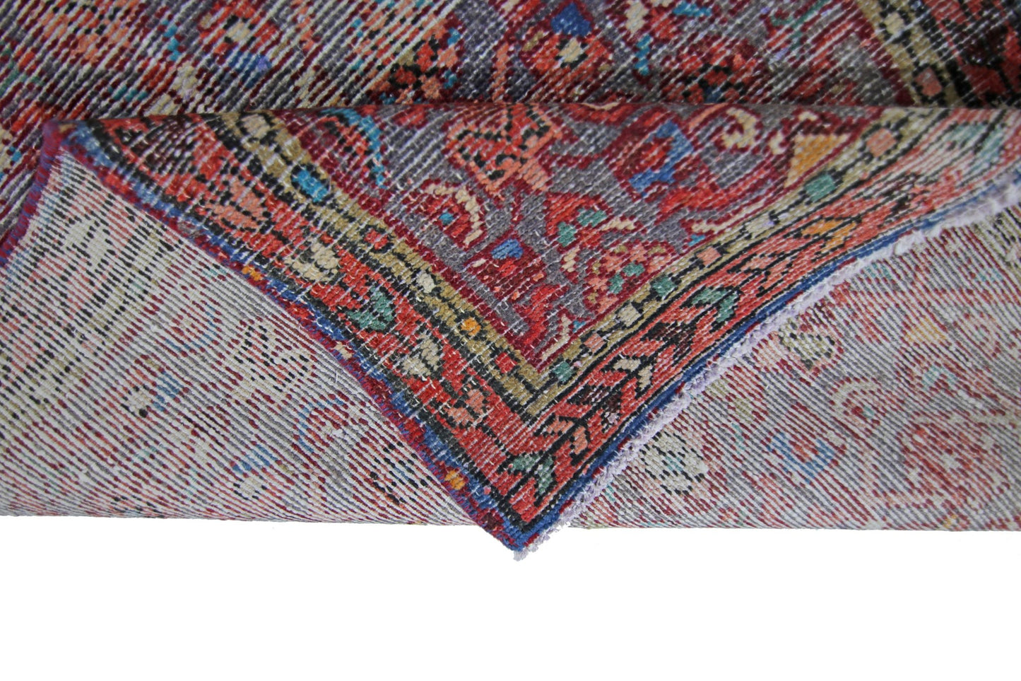 A folded vintage Persian rug featuring intricate red, blue, and yellow geometric patterns.