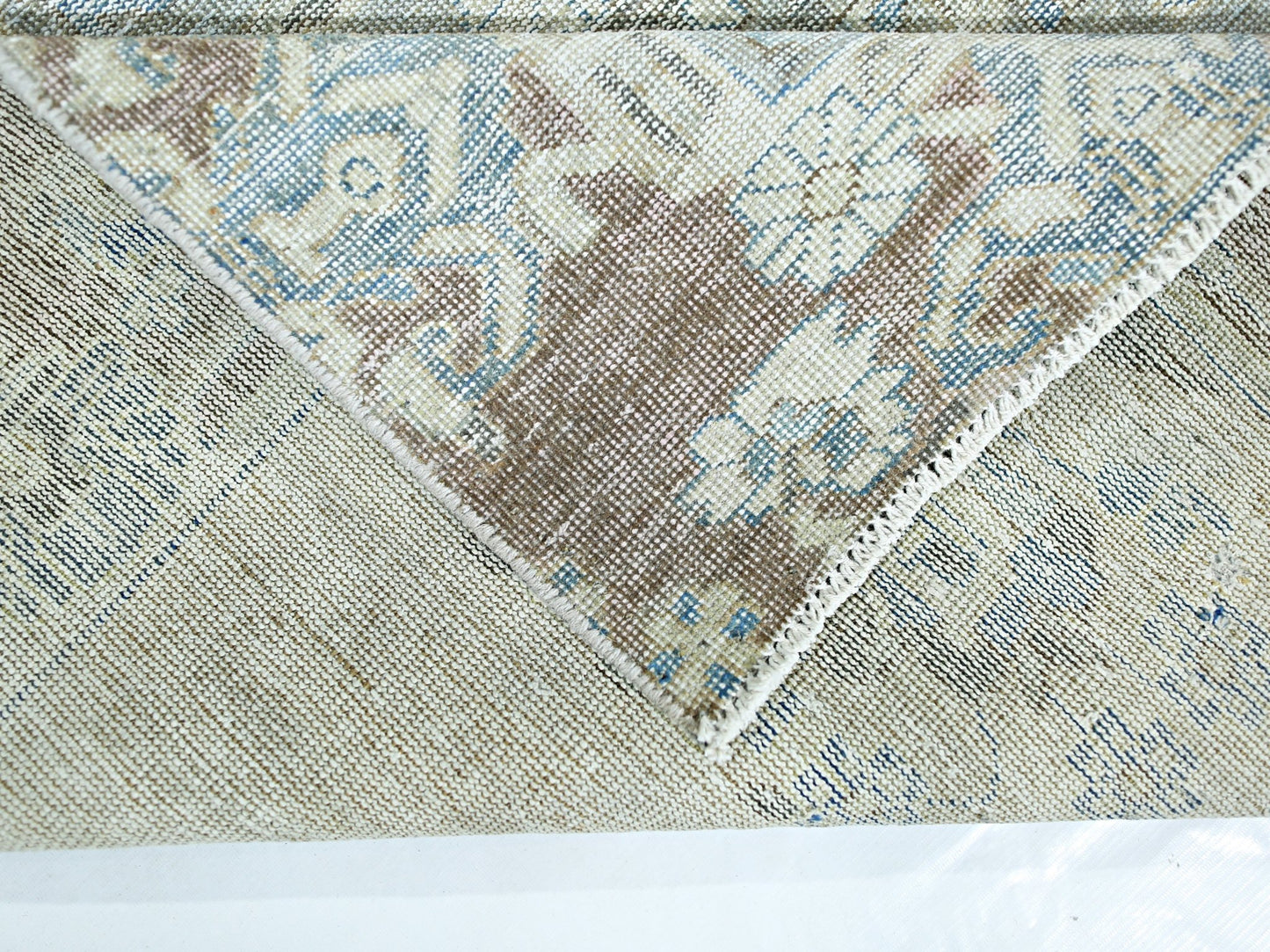 A folded corner of a vintage Persian rug showing a blue and brown floral pattern on wool.