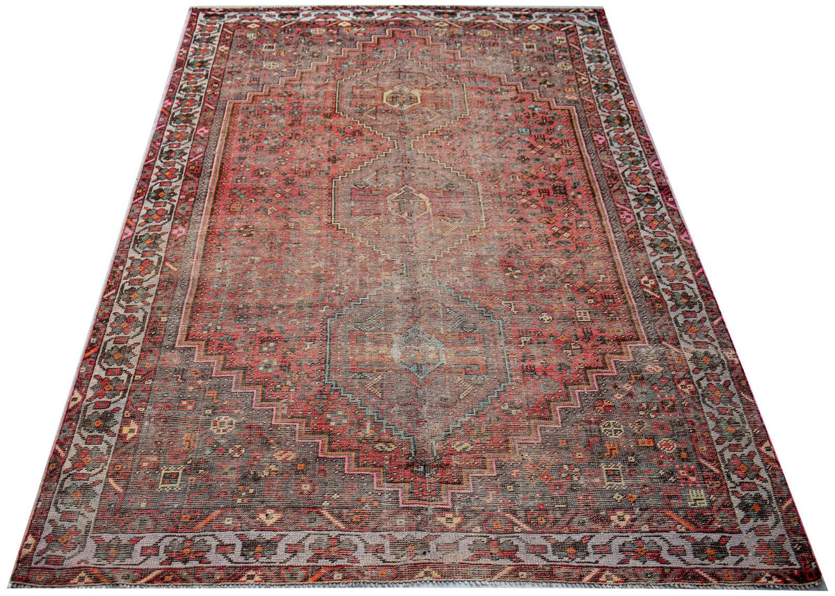 A handwoven vintage Persian rug featuring a faded red and grey geometric pattern.