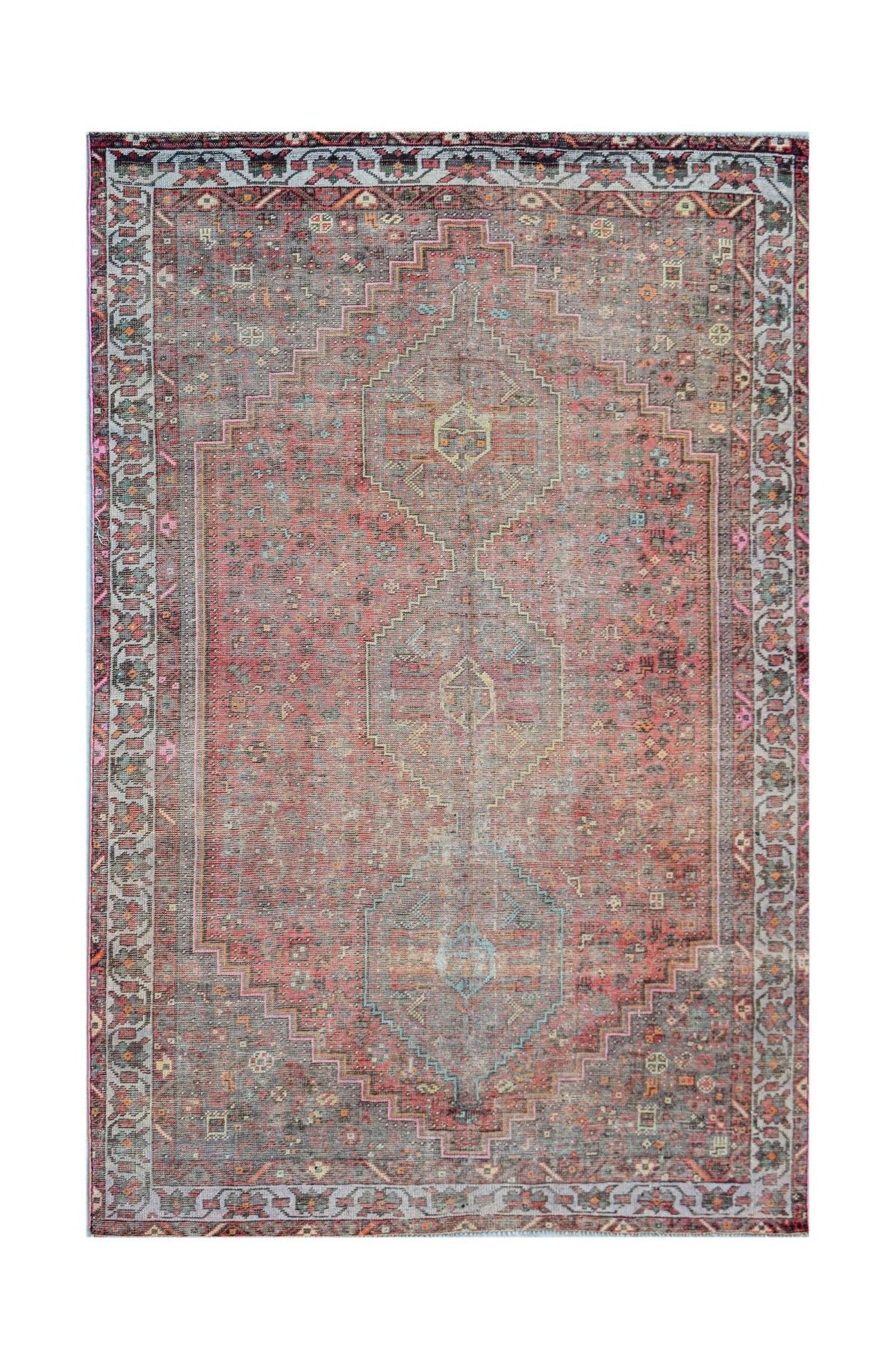 A vintage handwoven Persian rug featuring a faded red central medallion and intricate borders.